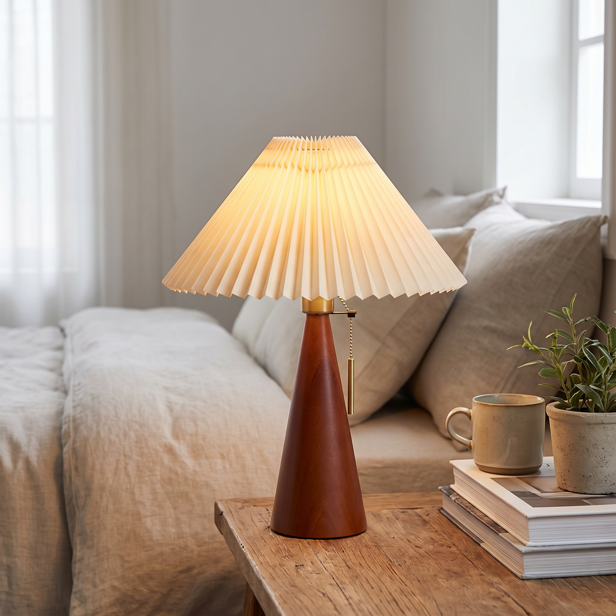 Japandi pleated table lamp with wood base shown lit on a bedside table