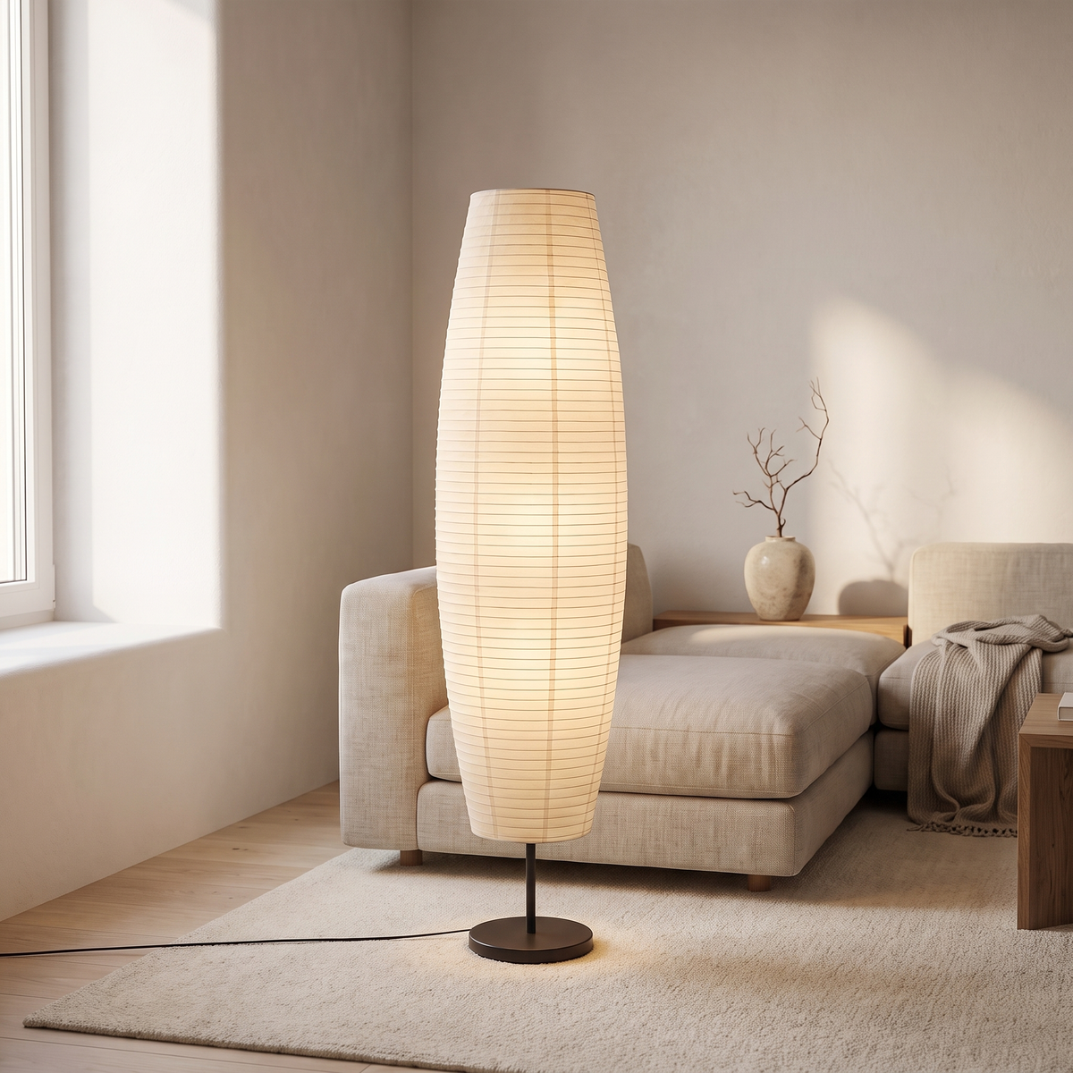 Rice paper column floor lamp lit in the corner of a Japandi living room beside a linen sofa