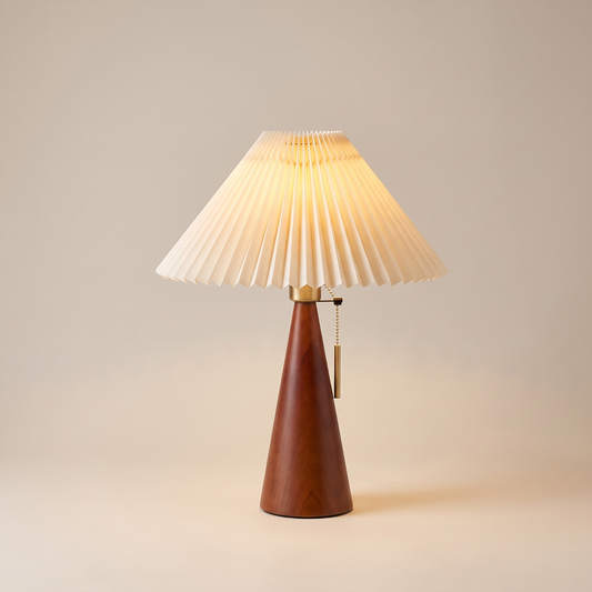 Japanese pleated fabric and wood table lamp, lit, on a warm neutral background