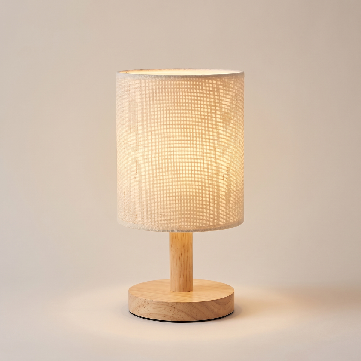 Fabric shade table lamp with bamboo wood base, lit, on a warm neutral background