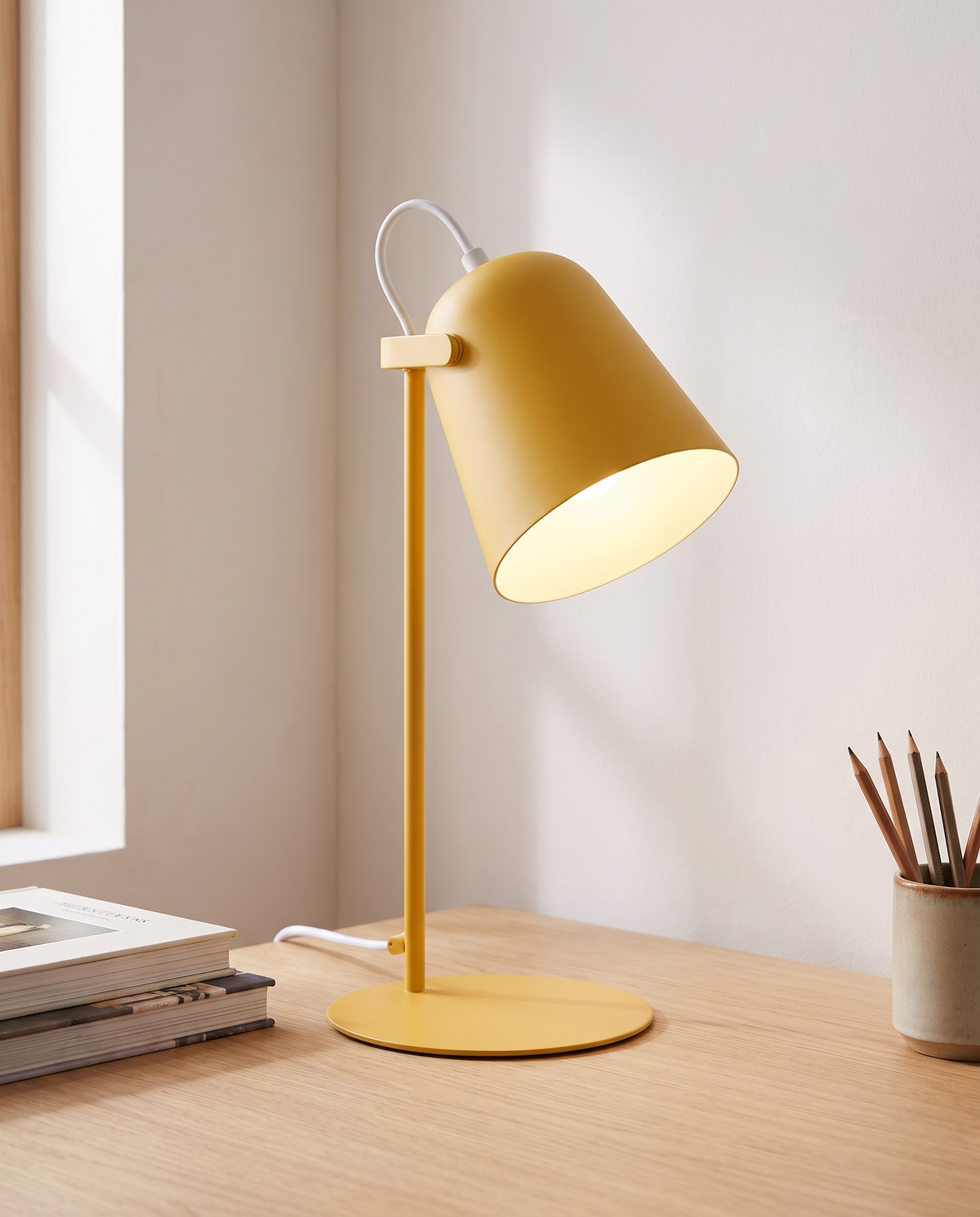 Yellow macaron iron bucket table lamp lit on a pale oak study desk